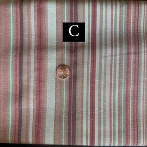 May include: Textile with vertical stripes in red, brown, and green. A penny is placed on the fabric for scale. A black square with the letter "C" is in the image.