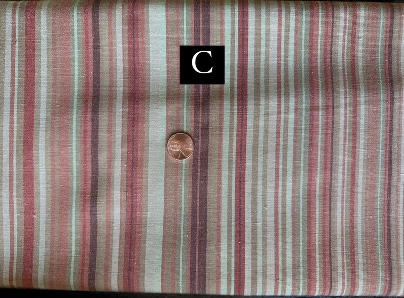 May include: Textile with vertical stripes in red, brown, and green. A penny is placed on the fabric for scale. A black square with the letter "C" is in the image.