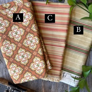 May include: Three folded fabric swatches with different patterns. One features a floral design in orange, brown, and green. Another has horizontal stripes in shades of orange and red. The third has green and red stripes on a beige background.