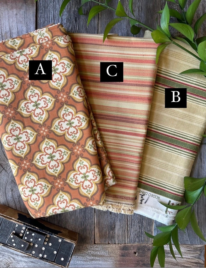 May include: Three folded fabric swatches with different patterns. One features a floral design in orange, brown, and green. Another has horizontal stripes in shades of orange and red. The third has green and red stripes on a beige background.