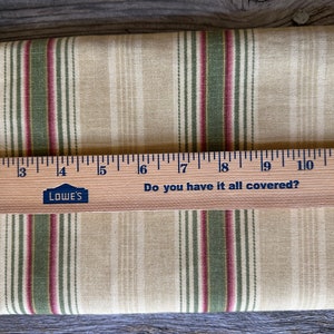May include: Beige fabric with green and burgundy vertical stripes. A wooden ruler with the text "Do you have it all covered?" and the Lowe's logo is placed across the fabric. The ruler measures up to 28 cm.