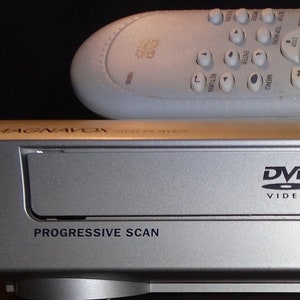 May include: A silver DVD player with a silver remote control. The DVD player has a slot for a disc, buttons for open/close, play, stop, power, and progressive scan. The remote control has buttons for various functions, including play, stop, and rewind.