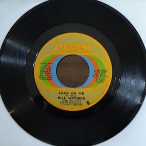 May include: A black vinyl record with a yellow and orange label. The label has the text "Sussex" in a stylized font. The record is titled "Lean On Me" by Bill Withers. The record number is "SUX 235".