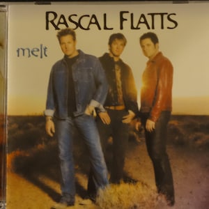 May include: A CD cover featuring a band called Rascal Flatts. The album cover is titled "melt" and features three men in a desert setting. The men are wearing casual clothing and are standing in front of a sunset.