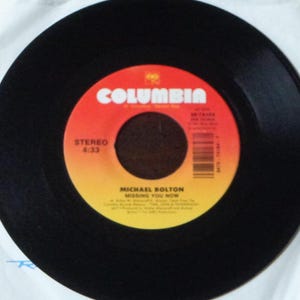 May include: A black vinyl record with a red and yellow label. The label features the word "COLUMBIA" in white, the text "STEREO 4:33", and the song title "MISSING YOU NOW" by Michael Bolton.