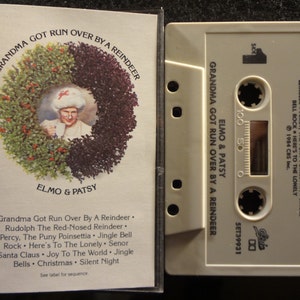 May include: A cassette tape with a white label featuring a cartoon image of Elmo and Patsy. The title of the cassette is "Grandma Got Run Over By A Reindeer" and the text on the label lists the songs included on the tape.