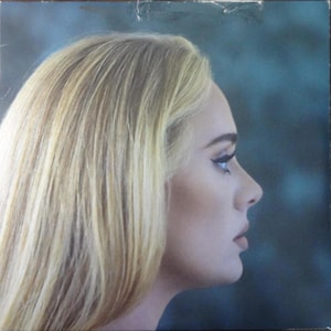May include: Album cover featuring a side profile of a person with blonde hair and a fair complexion. The person is looking to the right, with a dark eyeliner and a neutral lip color. The background is a gradient of blues and greens.