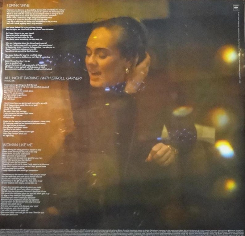 May include: Album cover featuring a woman with her hand near her head, with song lyrics visible. The album title is not visible. The background is dark with blurred lights. The album's song titles include "I Drink Wine", "All Night Parking (with Erroll Garner)", and "Woman Like Me".