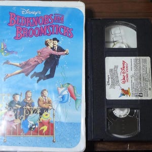 May include: A VHS tape and its case for Disney's "Bedknobs and Broomsticks." The case features a colorful illustration of characters floating in water. The VHS tape is black with a white label.