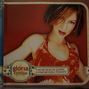 May include: A red and orange floral print halter top with the text "gloria estefan" and "no me dejes de querer como me duele perderte" on a white banner.
