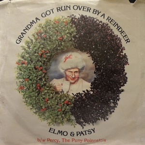 May include: A vintage album cover featuring a humorous illustration. The image shows a woman in a wreath with the text "GRANDMA GOT RUN OVER BY A REINDEER." The album title is "ELMO & PATSY" with "b/w Percy, The Puny Poinsettia" below.