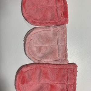 Op de afbeelding: Drie roze vierkante stoffen met een genaaide zak op elk. De stof is zacht en pluche.
