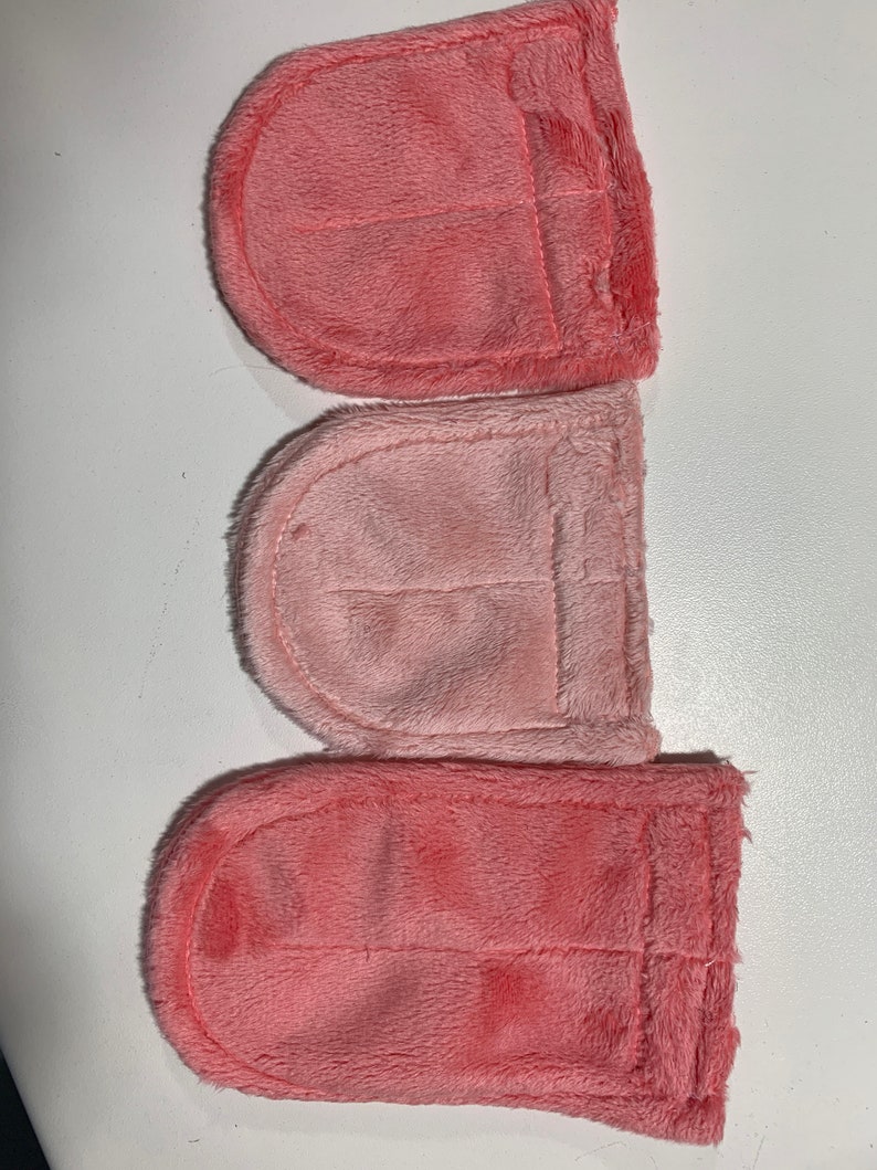 Op de afbeelding: Drie roze vierkante stoffen met een genaaide zak op elk. De stof is zacht en pluche.