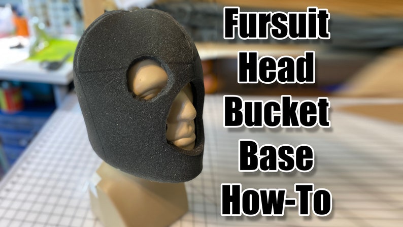 May include: A black foam head bucket base for a fursuit. The base has cutouts for the eyes and mouth. The text "Fursuit Head Bucket Base How-To" is visible in the background.