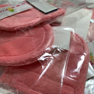 Op de afbeelding: Roze, pluche stoffen cirkels verpakt in doorzichtige plastic zakken. De stoffen cirkels hebben een zachte, pluche textuur.