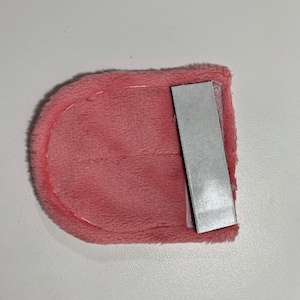 Op de afbeelding: Een roze pluche stoffen tasje met een transparant plastic venster en een grijze plakstrip aan de achterkant.