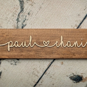 Puede incluir: Un letrero de madera con los nombres "paul" y "chani" escritos en cursiva con un s&iacute;mbolo de coraz&oacute;n entre ellos.