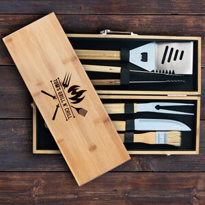 May include: A bamboo grilling set with a personalized engraved lid. The lid reads "Tom's Grill N Chill" with a grill, spatula, and fork graphic. The set includes a spatula, tongs, a grill brush, a fork, and a knife.
