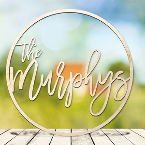 May include: A wooden circle with the text "The Murphys" in a cursive font. The circle is on a wooden surface with a blurred background of green and blue.