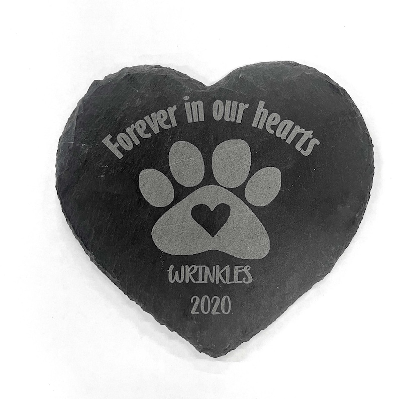 May include: Black heart-shaped slate stone with a paw print and a small heart inside the print. The text "Forever in our hearts" is above the paw print and the text "Wrinkles 2020" is below the paw print.