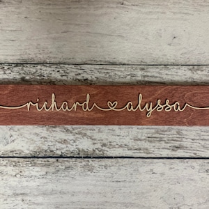 Puede incluir: Un letrero de madera con los nombres "richard" y "alyssa" escritos en cursiva con un s&iacute;mbolo de coraz&oacute;n entre ellos.