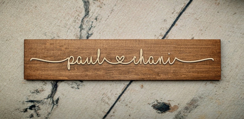 Puede incluir: Un letrero de madera con los nombres "paul" y "chani" escritos en cursiva con un s&iacute;mbolo de coraz&oacute;n entre ellos.