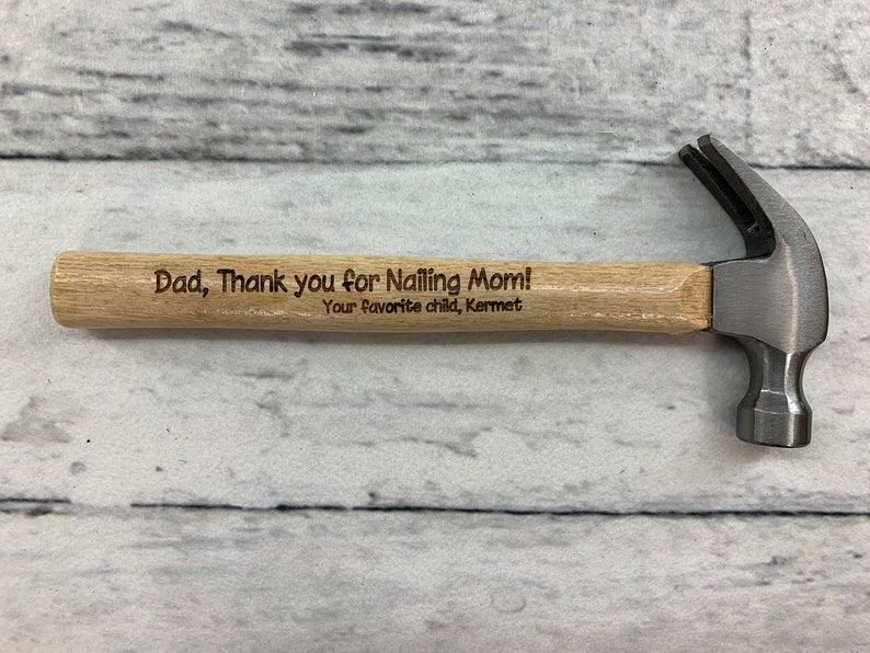 May include: A small wooden handled hammer with a metal head. The handle is engraved with the text "Dad, Thank you for nailing Mom! Your favorite child, Kermet".