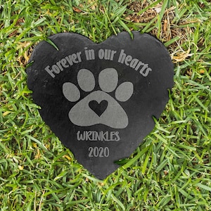 May include: A heart-shaped black slate memorial stone featuring an engraved paw print with a small heart in the center. The text Forever in our hearts is etched above the paw, with the name WRINKLES and the year 2020 engraved below the paw print.