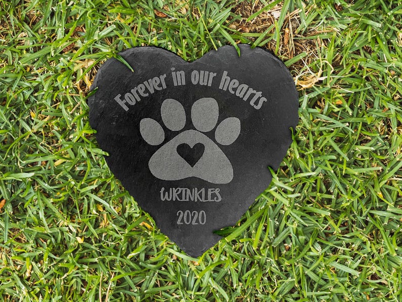 May include: A heart-shaped black slate memorial stone featuring an engraved paw print with a small heart in the center. The text Forever in our hearts is etched above the paw, with the name WRINKLES and the year 2020 engraved below the paw print.