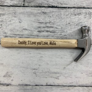 May include: A small wooden handled hammer with a metal head. The handle is engraved with the message "Daddy, I love you! Love, Malia".