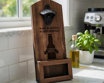 Puede incluir: Un abridor de botellas de pared de madera marrón oscuro con un abridor de metal negro en la parte superior. Presenta el texto I'M NOT AN ALCOHOLIC I'M A BEER ENTHUSIAST sobre un gráfico de botella con el nombre KEITHS en una cinta y una bandeja.
