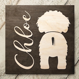 May include: A wooden sign with the name "Chloe" written in cursive and a cutout of a dog's rear end. The sign is dark brown with a light brown cutout.