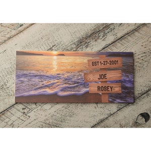 May include: A wooden sign with a beach sunset background. The sign has three lines of text: "EST 1-27-2001", "JOE", and "ROSE"Y.
