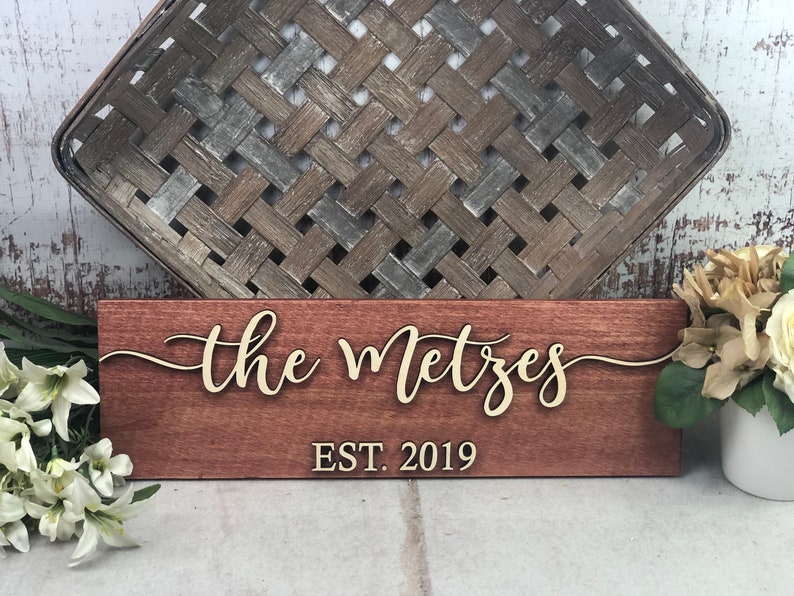 May include: A wooden sign with the text "the Metzes EST. 2019" in gold lettering. The sign is a dark reddish-brown color.