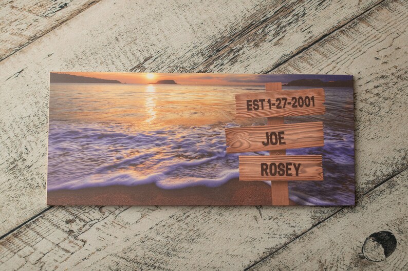 May include: A wooden sign with a sunset beach background. The sign has three wooden planks with the text "EST 1-27-2001", "JOE", and "ROSE" on them.