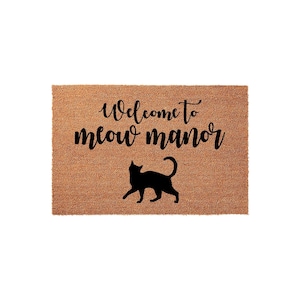 A textured doormat with the phrase "Welcome to meow manor" printed on it, along with a silhouette of a cat.