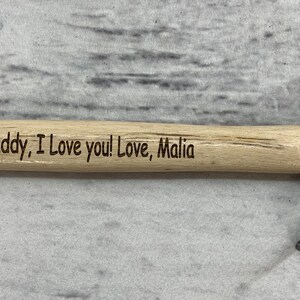 May include: A small wooden handled hammer with a metal head. The handle is engraved with the message "Daddy, I love you! Love, Malia".