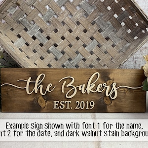 May include: A wooden sign with the text "the Bakers EST. 2019" in a cursive font. The sign is stained a dark walnut color.
