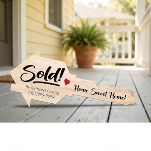May include: A light-colored wooden sign shaped like a large house key. The text reads Sold! By Richard Castle (501)999-9999 and Home Sweet Home! with a small red heart icon. The sign features a natural wood grain finish and black lettering.
