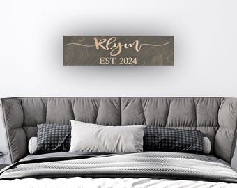 May include: A rectangular dark brown wooden sign with a visible wood grain texture. The sign features the name Klym in a light-colored cursive script font, with the text EST. 2024 printed in a simple sans-serif font directly underneath.