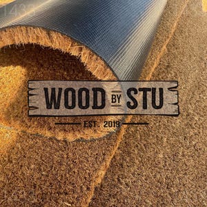 a close-up of a textured surface, possibly a carpet or mat, with a logo or text overlay in the center.