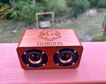 May include: A wooden speaker with a personalized engraved design. The speaker is red and has two black speakers. The engraving includes the letter "G" inside a circle with antlers and the name "GORDON".