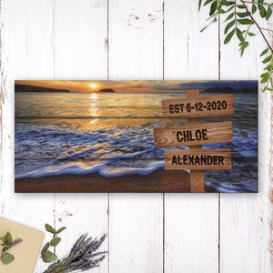 May include: A panoramic photograph of a beach sunset with three wooden signs. The top sign reads "EST 6-12-2020", the middle sign reads "CHLOE", and the bottom sign reads "ALEXANDER".