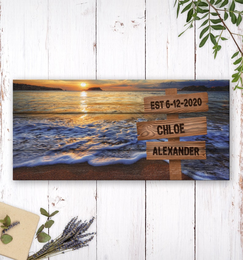 May include: A panoramic photograph of a beach sunset with three wooden signs. The top sign reads "EST 6-12-2020", the middle sign reads "CHLOE", and the bottom sign reads "ALEXANDER".