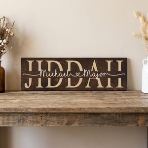 May include: A dark brown wooden sign with the names "Michael" and "Major" in a cursive font, separated by a heart symbol. The names are centered on the sign, with the last name in a larger font. The sign is displayed on a rustic wooden table.