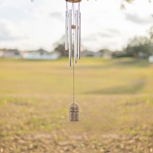 May include: Silver wind chime hanging from a tree branch with a wooden tag that reads "Never underestimate the difference one life can make."  John E. Marston
