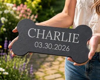 Puede incluir: Una placa negra con forma de hueso y superficie texturizada que presenta el nombre grabado CHARLIE y la fecha 03.30.2026 en una fuente gris claro sin remates. La placa se sostiene horizontalmente, mostrando un contraste claro entre el material oscuro y el texto.