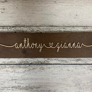 Puede incluir: Un letrero de madera con los nombres "anthony" y "gianna" escritos en cursiva con un s&iacute;mbolo de coraz&oacute;n entre ellos.