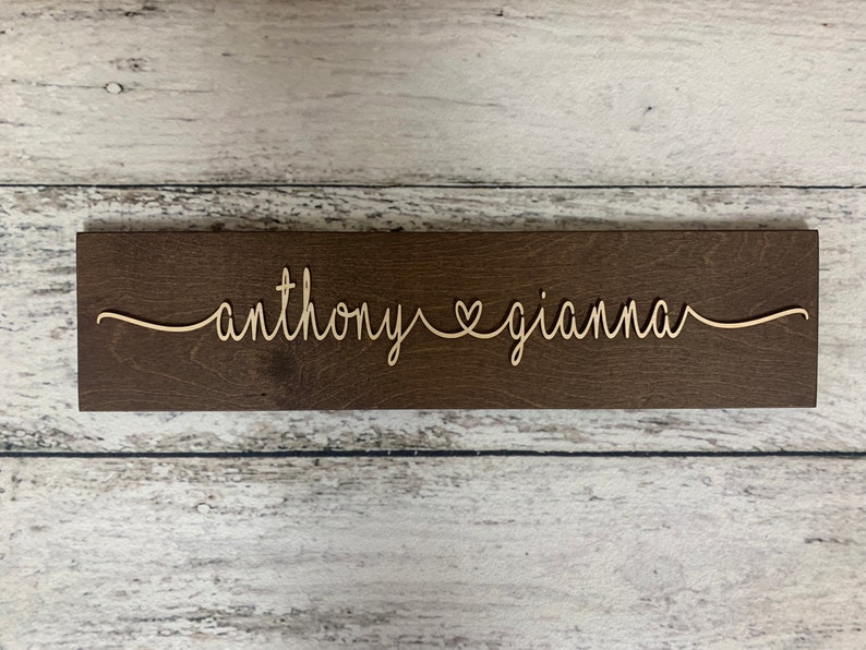 Puede incluir: Un letrero de madera con los nombres "anthony" y "gianna" escritos en cursiva con un s&iacute;mbolo de coraz&oacute;n entre ellos.