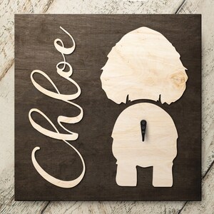 May include: A wooden sign with the name "Chloe" cut out in a cursive font. The sign also features a cutout silhouette of a dog's rear end.